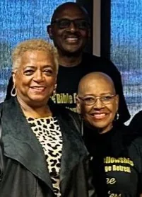 Three people smiling together at an indoor event with blue lighting in the background
