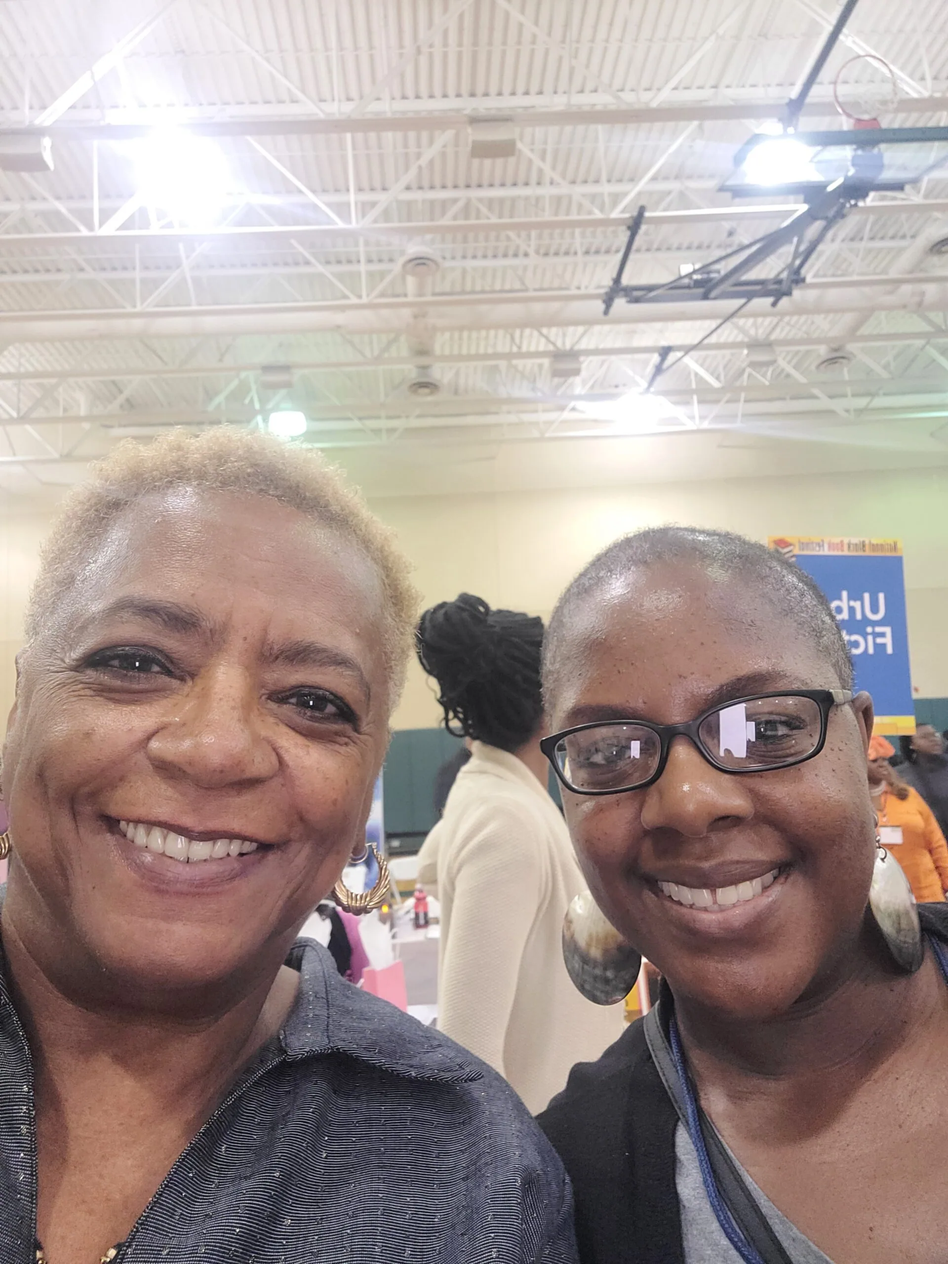 Two smiling women at an indoor event with industrial ceiling and lights visible in background